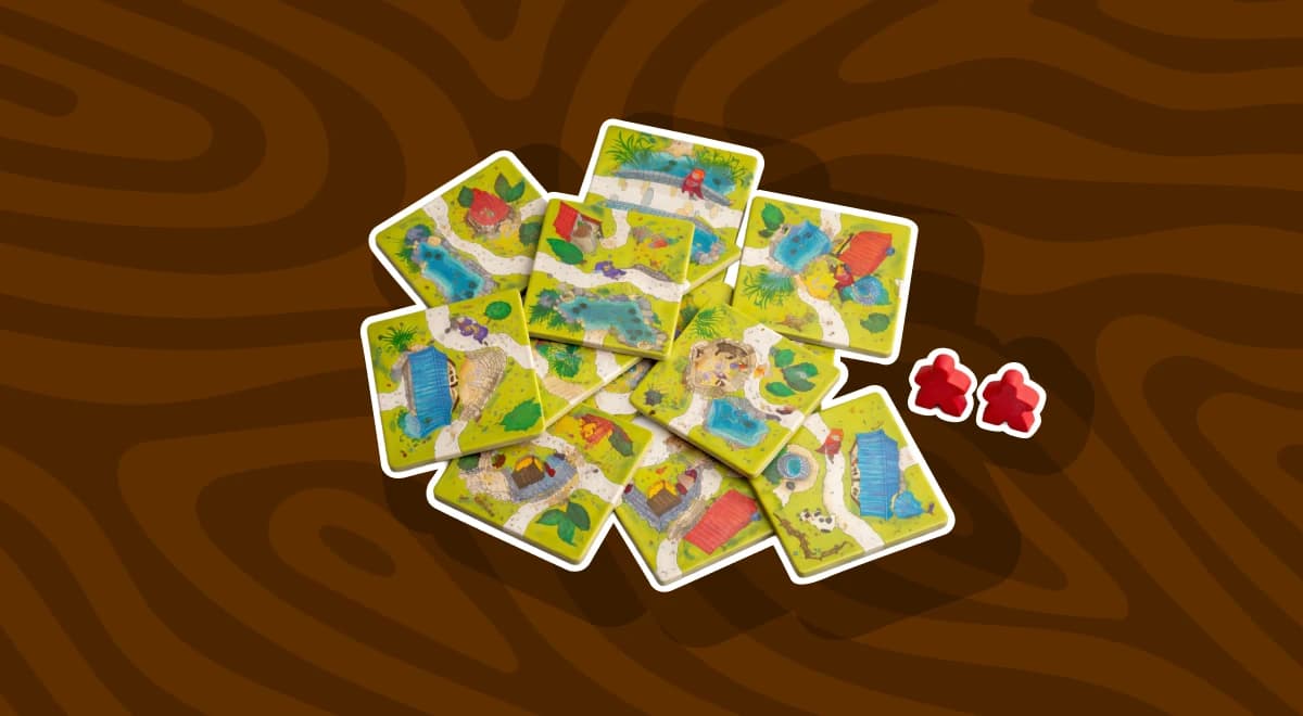 Scattered Carcassonne board game tiles with illustrated landscapes and two red meeple pieces on a dark brown wooden surface