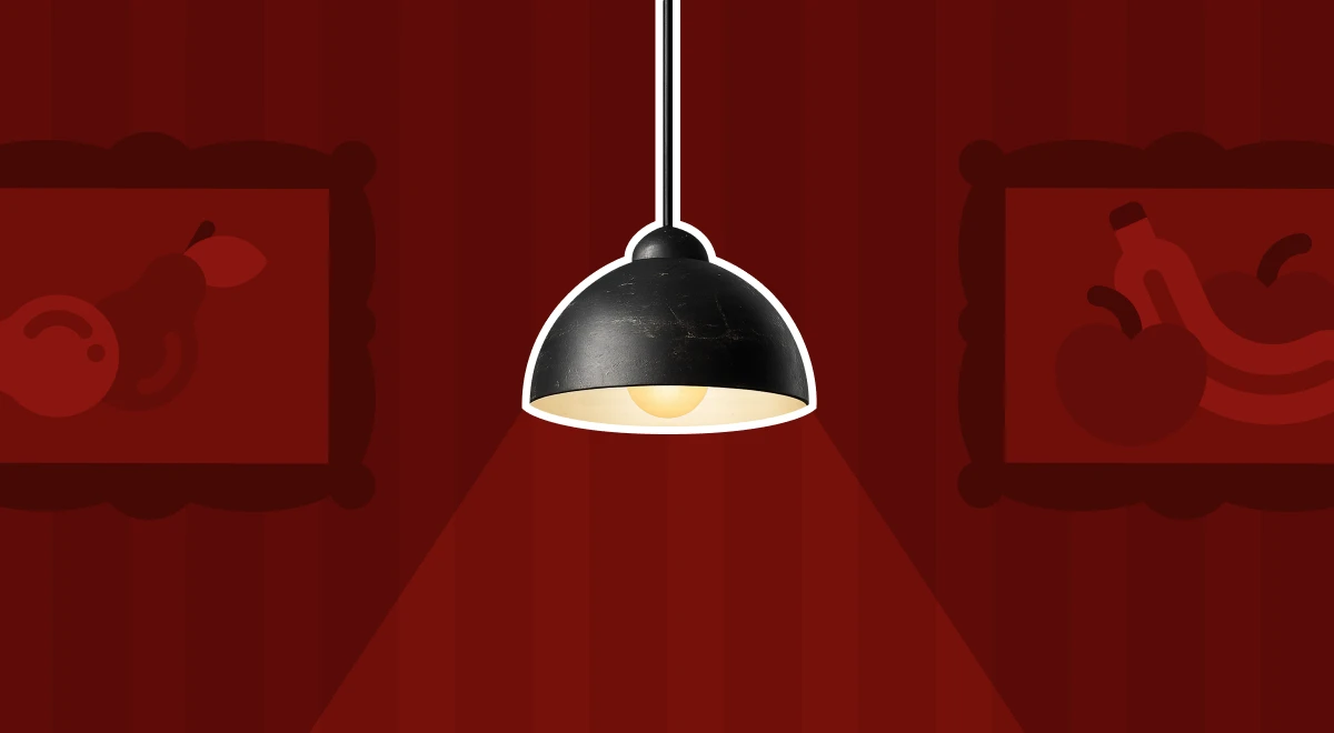 Black pendant lamp casting warm light downward against a dark red background with framed decorative wall art on both sides